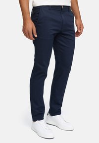 Mørkeblå bukser i bomuldsblanding med slim fit, der har frontlommer og lynlås, parret med hvide sneakers med lavt skaft.
