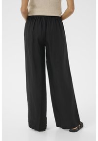 Zwarte wijde broek gemaakt van lichtgewicht stof, met een elastische tailleband en een vloeibare silhouette. Gecombineerd met zwarte platte sandalen.