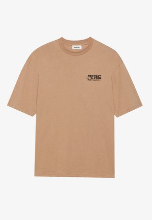 Beige pamut póló laza szabással, kerek nyakkivágással és rövid ujjal. Az elején fekete felirat található: "TÖKÉLETES ÖSSZEILLESZTÉS."