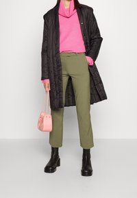 Černý prošívaný dlouhý kabát, růžový žebrovaný svetr, olivově zelené kalhoty, černé platformové boty a malá růžová kabelka. Texturované vrstvy a barvy.