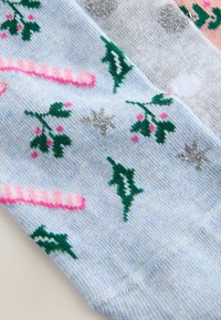 Blue knitted socks featuring patterns of pink candy canes, green holly leaves, silver snowflakes, and multicolored accents.