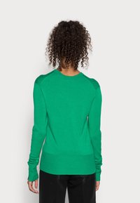 Vihreä neulepusero, jossa on pitkät hihat, ribbireunat ja pyöreä kaula-aukko; siinä on sileä koostumus ja istuva siluetti.