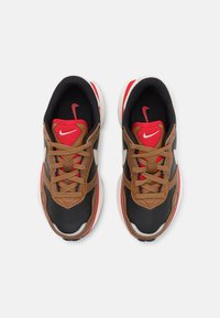 Nike sneakers feature a black mesh upper, brown leather accents, red details, and a white midsole. Laces and logo are included in matching tones.