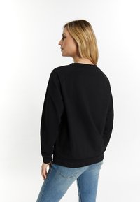 Felpa nera a maniche lunghe con collo rotondo e maniche raglan. Texture liscia con una vestibilità rilassata. Abbinata a jeans azzurri.