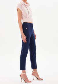 Blusa a righe rosa croppata con maniche corte; pantaloni blu fitted con tasche laterali; sandali bianchi con tacco alto e cinturino.