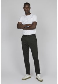 Camiseta blanca de manga corta combinada con pantalones ajustados verdes y zapatillas blancas con acentos en gris y oliva. Diseño simple y moderno.