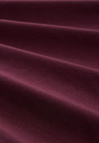 Gładki, miękki materiał w głębokim burgundowym kolorze z subtelnymi poziomymi fałdami, które tworzą delikatne cienie i teksturę.