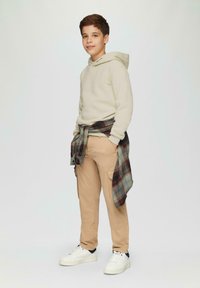 Beige hoodie, khaki cargobroeken, geruit overhemd om de taille geknoopt, witte sneakers met marineblauwe accenten, relaxte pasvorm, gladde stof.