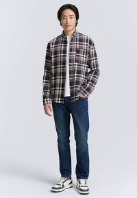Męska flanelowa koszula w kratę w odcieniach granatu, czerwieni i bieli, z długimi rękawami, kieszenią na piersi, zestawiona z niebieskimi dżinsami i wzorzystymi trampkami.