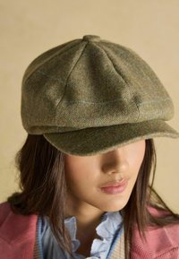 Zelená čiapka s rybinovým vzorom, zaoblenou, štruktúrovanou korunou a širokou krempou. Vzorku zdobia svetlomodré a ružové akcenty.