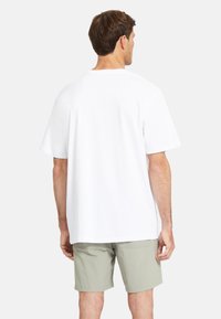 T-shirt bianca in cotone con maniche corte, collo a giro e vestibilità rilassata, abbinata a pantaloni corti verdi chiari, vista da dietro.
