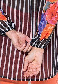 Camicia a maniche lunghe con righe verticali bianche e nere, corpo bordeaux e vivace stampa floreale sulle maniche. Dettaglio con polsini elasticizzati ai polsi.