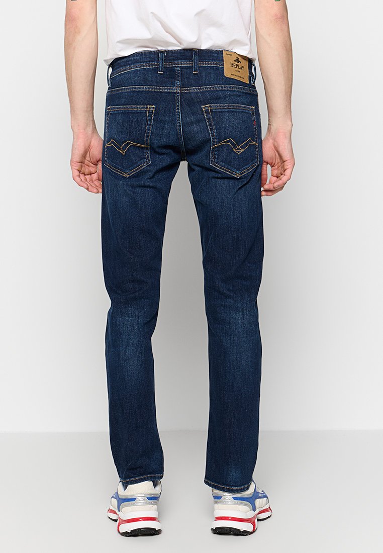 Jeans in denim blu scuro con vestibilità dritta, dotati di una patch in pelle marrone con marchio, cuciture gialle in contrasto e due tasche posteriori.