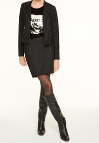 Chaqueta negra con cremallera sobre una camiseta negra con lentejuelas, combinada con una falda negra texturizada y botas de cuero hasta la rodilla.