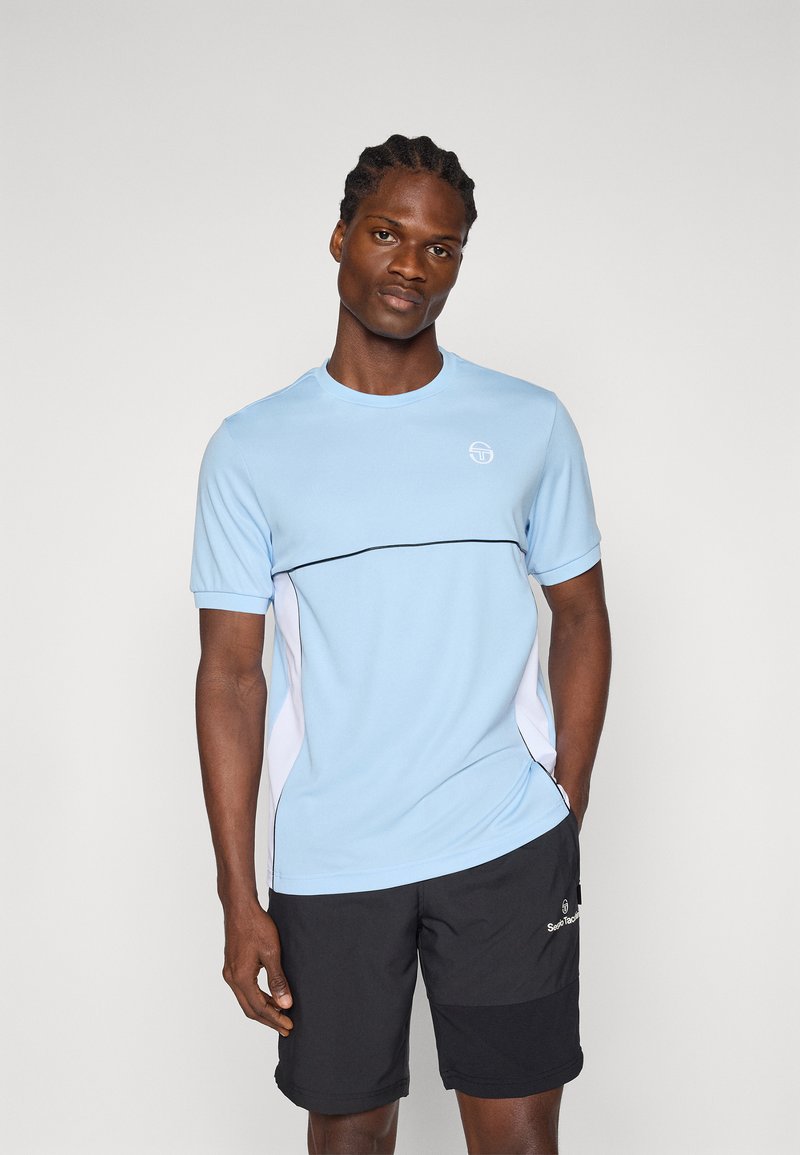 Camiseta deportiva de color azul claro con mangas cortas, ribete negro y acentos laterales blancos; llevada con pantalones cortos negros que presentan un logo.
