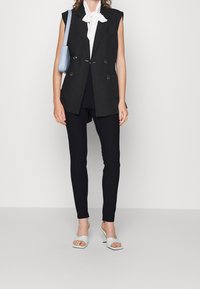 Svart dubbelknäppt ärmlös blazer över en vit blus, parat med svarta slim fit-byxor och ljusblå öppna klackar.