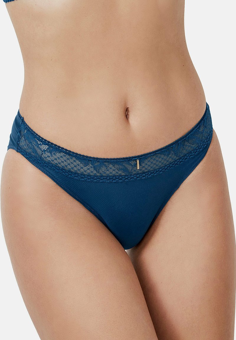 Bas de bikini bleu marine avec une bordure en dentelle au niveau de la ceinture, un tissu doux et un subtil accent métallique à l'avant.