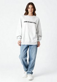 Szürke pulóver fekete felirattal: "INKÁBB RAKÉTATUDOMÁNYRA KEDVELEM," laza fazonú, bordázott mandzsettákkal és puha tapintású. Világoskék farmernadrággal párosítva.