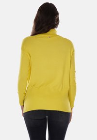 Maglione giallo a collo alto con trama a coste, maniche lunghe e vestibilità rilassata, che presenta un piccolo logo sul retro.