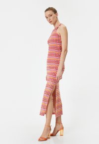 Figurbetontes, ärmelloses Kleid mit mehrfarbigen Mustern in Pink, Rot und Orange, mit Seitenschlitzen und einer glatten, strukturierten Oberfläche.