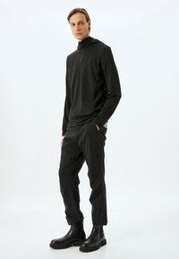 Sort langærmet top med høj krave, parret med sorte sweatpants og sorte ankelstøvler, der har lige ben og sidelommer.