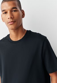 Juoda medvilninė marškinėlių su apvalia kaklo iškirpte ir trumpomis rankovėmis. Lygus paviršius, laisvas siluetas, minimalistinis dizainas be matomų logotipų ar raštų.