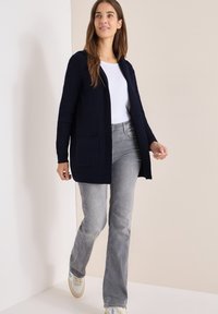 Granatowy sweter z dzianiny, z długimi rękawami, otwarty z przodu, o prążkowanej strukturze, z dwiema kieszeniami z przodu; noszony na białej bluzce i szarych dżinsach.