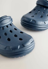 Blå gummitofflor med perforeringar för ventilation, en texturerad yta och en tjock, upphöjd sula för hållbarhet.