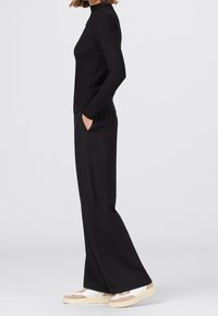 Svart ribbad långärmad topp kombinerad med vida svarta byxor och sneakers med beige och vita detaljer, visad från sidan.