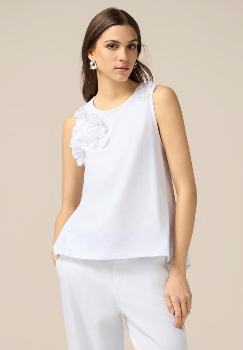 Top bianco senza maniche con accenti floreali testurizzati sulla spalla sinistra, realizzato in tessuto liscio con una vestibilità rilassata e scollatura tonda.
