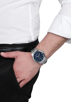 Orologio in acciaio inox argentato con quadrante blu, movimento al quarzo, display della data e bracciale argentato, indossato su un polso chiuso.