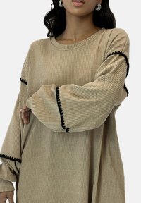 Beige ribbad tröja med långa ärmar, med svarta vågiga detaljer längs ärmsluten, texturerad tyg och en avslappnad passform.