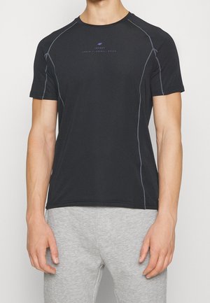 Sort atletisk t-shirt med korte ærmer og grå syningsdetaljer, båret af en person i lysegrå shorts, beskåret ved nakke og knæ.