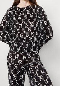 Set coordinato di top e pantaloni in bianco e nero con un mix di disegni geometrici e astratti, texture plissettata e vestibilità comoda.