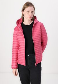 Padded pink jacket with a hood, featuring a quilted design and a front zipper. Worn over a black top and paired with black pants.
