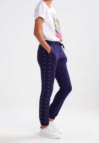 Navy jogger pants with a drawstring waist and metallic studs along the sides, paired with a short-sleeve graphic t-shirt and white sneakers.