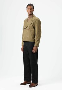 Olijfgroene double-breasted jas met grote knopen, gecombineerd met donkere, wijde jeans en bruine leren schoenen. Lichtgewicht stof, gestructureerde pasvorm.