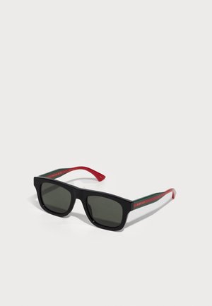 Black sunglasses with green and red striped arms. Square frames and dark lenses. Features "GUCCI" branding in red on the inner side of the arm.
