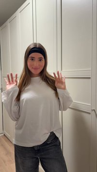 Camicia bianca a maniche lunghe con dettaglio nodo in vita, abbinata a jeans grigio scuro. Una fascia nera completa il look.