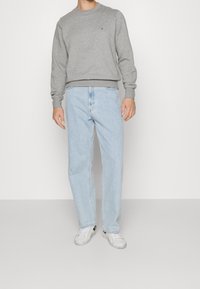 Szara bluza z prążkowanymi mankietami i ściągaczem u dołu, jasnoniebieskie jeansy o prostych nogawkach oraz białe sneakersy z czarnymi dodatkami, widoczne od pasa w górę.