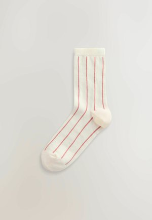 Balta kojinė su rožinėmis vertikaliomis juostelėmis, ribuotu aulu, nesiūlėtu pirštu ir lygiu paviršiumi. Dizainą puošia vientisas rožinis kulnas ir piršto detalės.