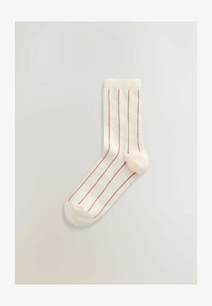 Balta kojinė su rožinėmis vertikaliomis juostelėmis, ribuotu aulu, nesiūlėtu pirštu ir lygiu paviršiumi. Dizainą puošia vientisas rožinis kulnas ir piršto detalės.