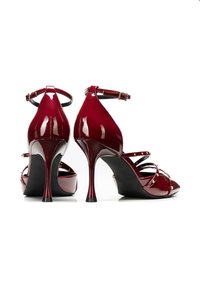Décolleté rossa in vernice con punta affilata, sottile cinturino alla caviglia e cinturini decorati. Presenta un tacco a stiletto e un design con platform.