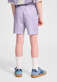 Lavendelshorts med elastiskt midjeband, kombinerade med blå sneakers och vita strumpor, visande bakvy och slät tygtextur.
