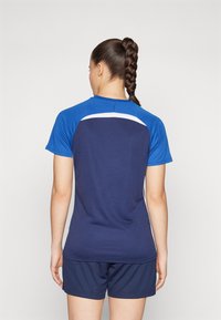 Marine atletisk skjorte med korte ærmer og en blå skulderdetalje, parret med matchende marineblå shorts. Glat tekstur, sporty design.