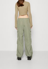 Korte beige textuur top gecombineerd met loszittende, lichtgroene cargo pants met zijzakken en elastische manchetten. Zwarte laarzen zichtbaar.