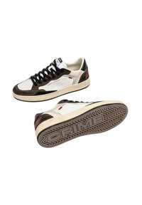 Sneaker basse in suede bianco e marrone con lacci neri, marchiate "CRIME LONDON", una scarpa mostra la suola decorata con il testo "CRIME".
