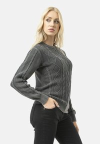Grey knitted sweater featuring cable and diamond patterns, ribbed cuffs and hem, and a round neckline. Worn over black pants.