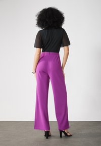 Top nero con maniche corte trasparenti abbinato a pantaloni viola a vita alta e gamba larga. Tessuto morbido e silhouette aderente in vita.