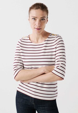Camicia a strisce bianche con righe orizzontali color borgogna, collo rotondo, maniche a tre quarti e bottoni decorativi dorati sulla spalla.